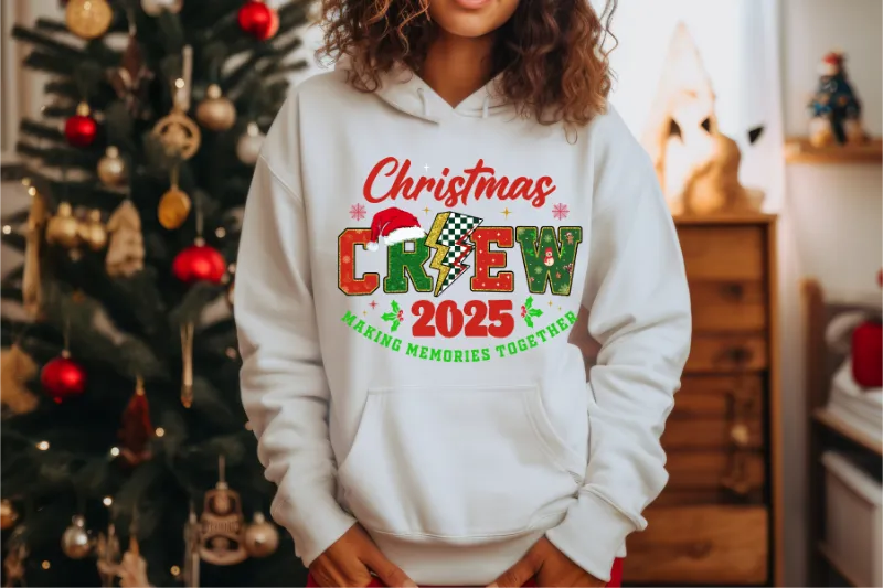 White hoodie with Christmas Crew 2025 design, decorated Christmas tree in background