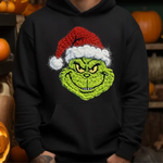 Green grinch character with santa hat printed on black hoodie surrounded by halloween pumpkins