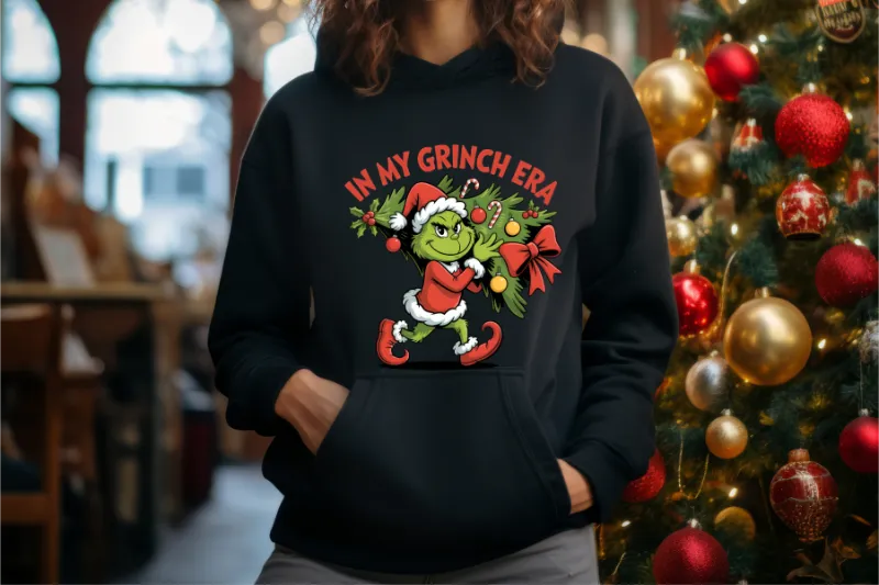 Black hoodie with In My Grinch Era Christmas design featuring cartoon Grinch in Santa outfit