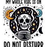 "MY WHOLE VIBE IS ON DO NOT DISTURB" Illustration of a stylized skull holding a mug, surrounded by crescent moons, stars, and crosses on a black background, creating a mystical, whimsical aesthetic.