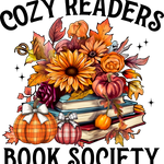 The text reads "COZY READERS BOOK SOCIETY". The image depicts a stack of books surrounded by autumn-themed elements: sunflowers, pumpkins with bows, maple leaves, roses, and sparkling stars, creating a warm, inviting reading atmosphere.