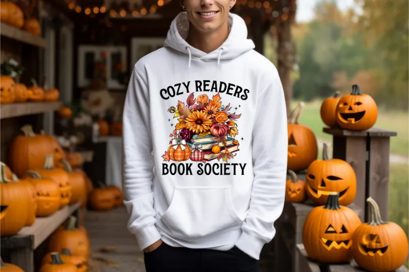 White hoodie with Cozy Readers Book Society design featuring autumn flowers, books, and pumpkins