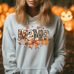 White hoodie with Mama text design featuring pumpkins, autumn leaves, and bow against jack-o-lantern background