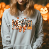 White hoodie with Mama text design featuring pumpkins, autumn leaves, and bow against jack-o-lantern background