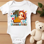 White baby onesie with colorful My 1st Thanksgiving design featuring turkey, leopard number 1, and autumn leaves