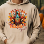 Cream hoodie with colorful turkey design featuring Stay Blessed Yall text and autumn leaves, with pumpkins in background