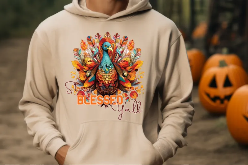 Cream hoodie with colorful turkey design featuring Stay Blessed Yall text and autumn leaves, with pumpkins in background