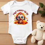 White baby onesie with cute cartoon turkey graphic, surrounded by autumn leaves and pumpkins