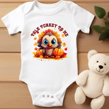 White baby onesie with cute cartoon turkey graphic, surrounded by autumn leaves and pumpkins